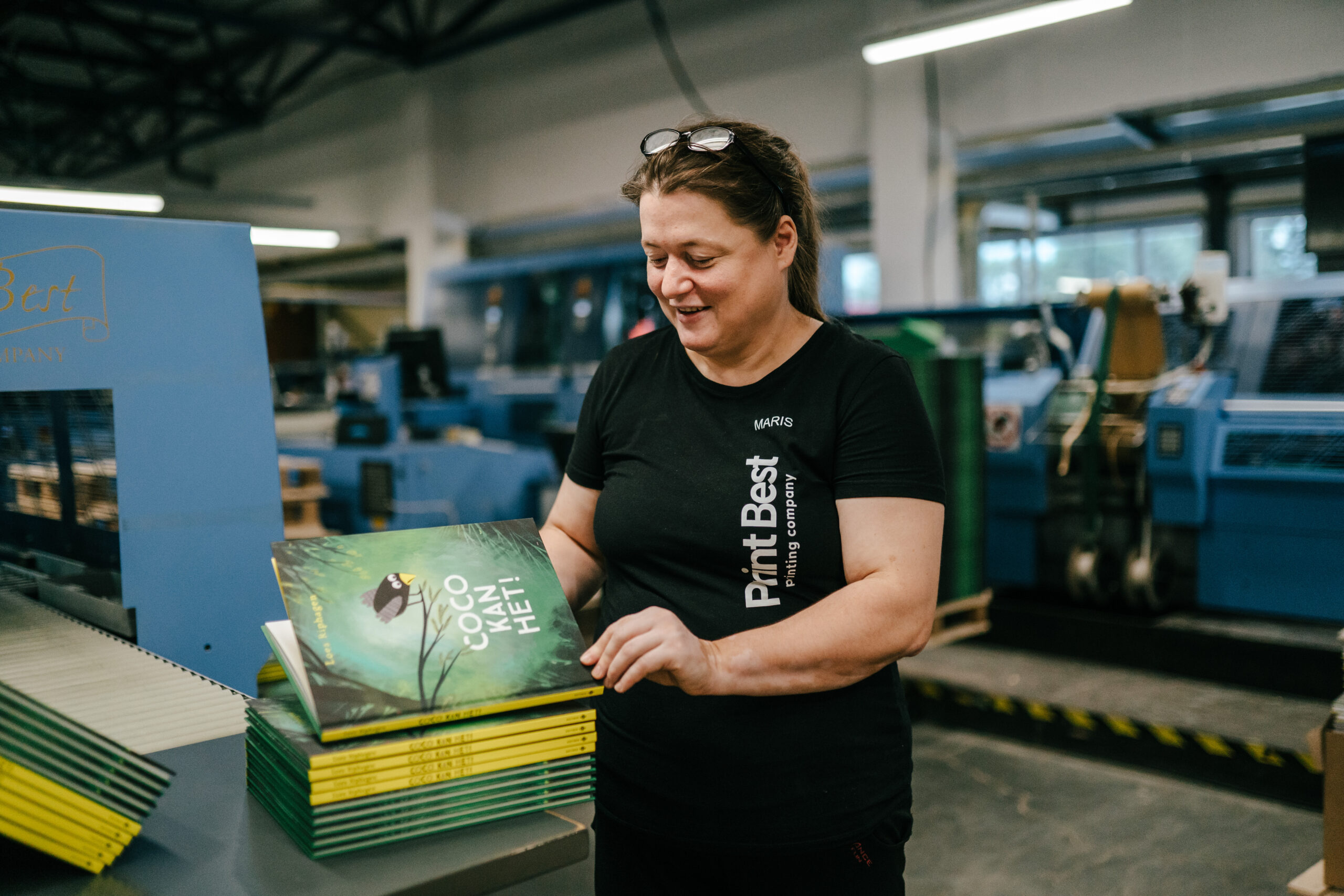 What We Value Print Best employee inspecting freshly printed hardcover children's books in a modern book production facility in Estonia.